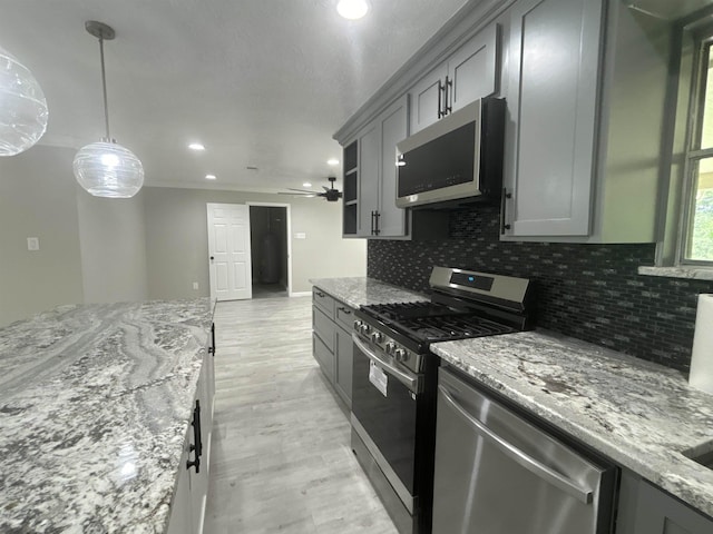 kitchen featuring gray cabinets, pendant lighting, decorative backsplash, light stone countertops, and appliances with stainless steel finishes