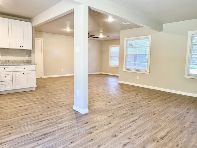 interior space with light wood-type flooring, white cabinetry, ceiling fan, and light stone counters