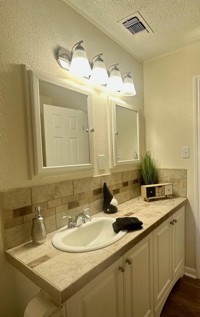 401 Camellia Ave, Orange, TX 77630 - bathroom with a textured ceiling, backsplash, a textured wall, vanity, and wood finished floors