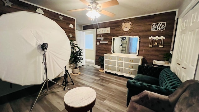 sitting room with ornamental molding, hardwood / wood-style flooring, ceiling fan, and wooden walls