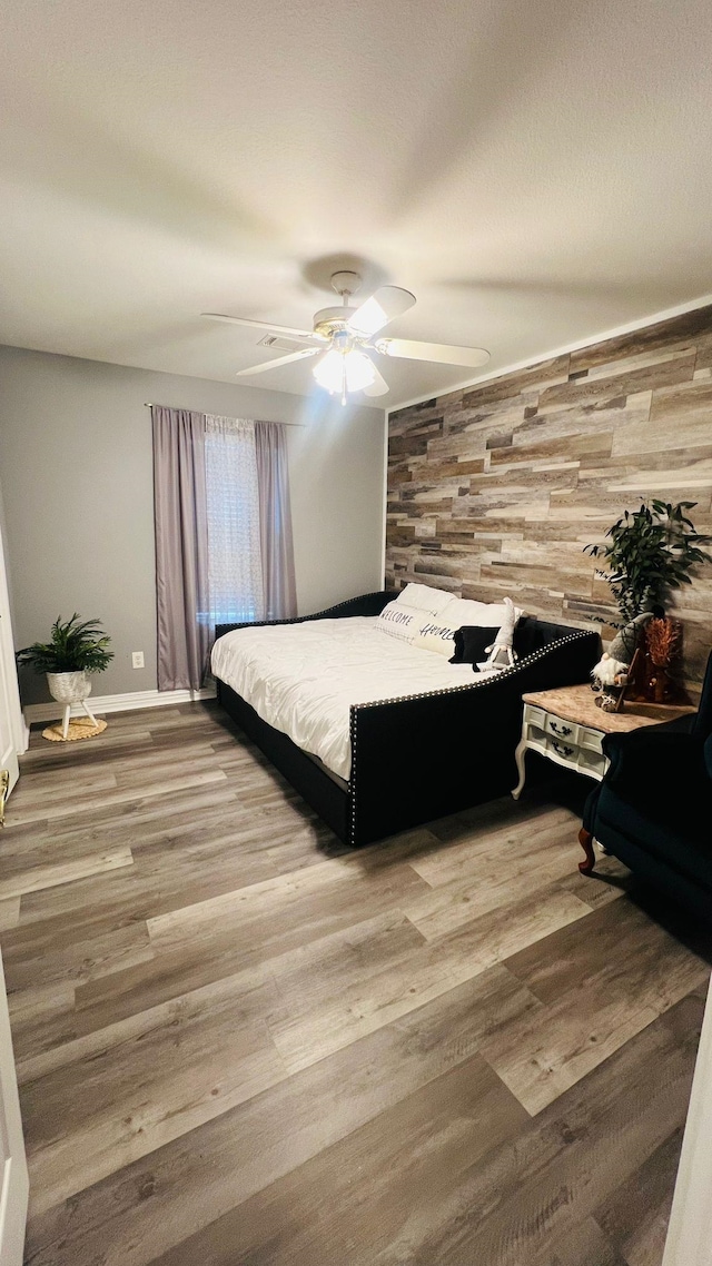 bedroom featuring hardwood / wood-style floors, ceiling fan, and wooden walls