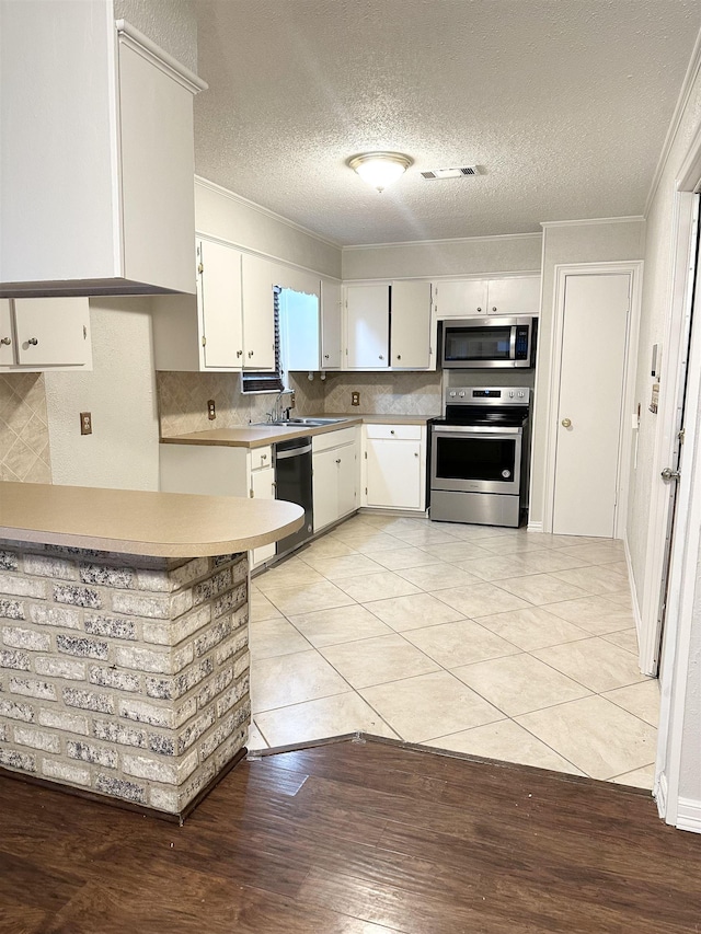 kitchen with appliances with stainless steel finishes, backsplash, a textured ceiling, white cabinetry, and light tile patterned flooring