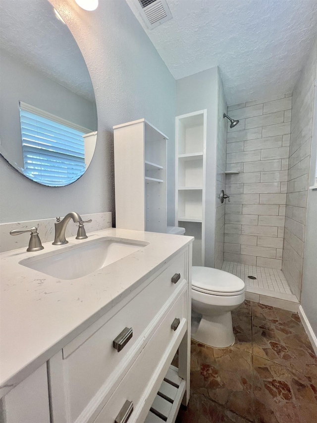 bathroom featuring vanity, toilet, a textured ceiling, and a tile shower