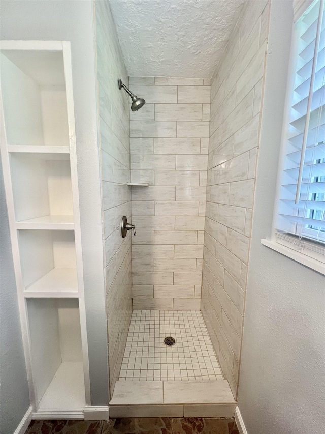 bathroom with a tile shower, a textured ceiling, and built in shelves