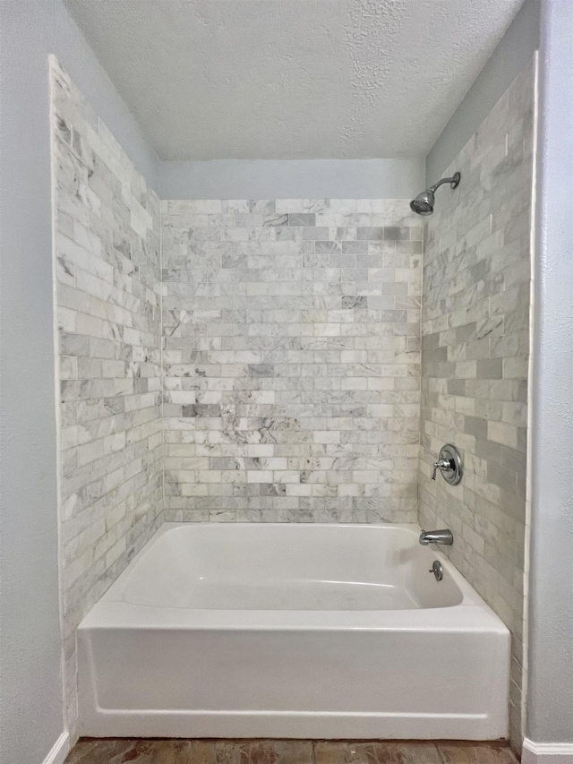 bathroom with a textured ceiling and tiled shower / bath