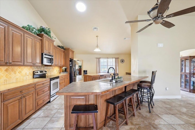 kitchen with sink, a kitchen breakfast bar, decorative backsplash, stainless steel appliances, and a center island with sink