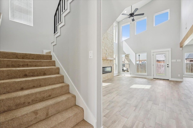 stairway with wood finished floors, a towering ceiling, a fireplace, baseboards, and ceiling fan