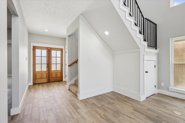 foyer entrance featuring light wood finished floors, french doors, a textured ceiling, and stairs