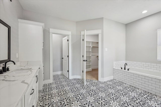 full bath with baseboards, vanity, a bath, and a spacious closet