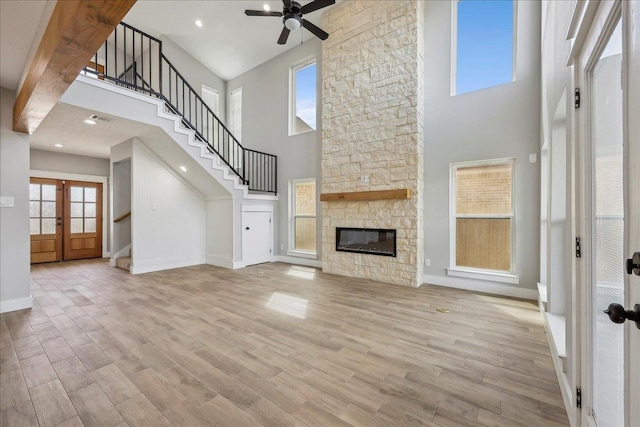 unfurnished living room with stairway, baseboards, light wood-style flooring, a fireplace, and french doors