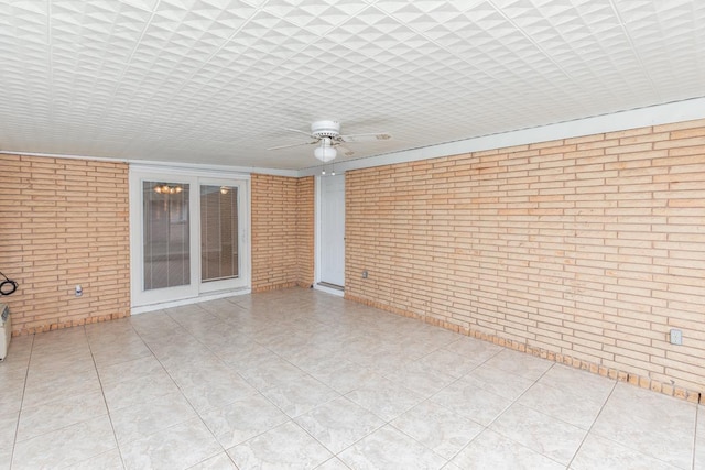 empty room featuring ceiling fan and brick wall