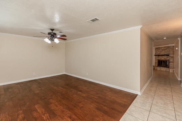 spare room featuring ceiling fan, ornamental molding, a textured ceiling, and a brick fireplace