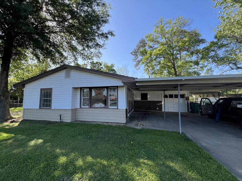 ranch-style house with a carport, an attached garage, driveway, and a front lawn