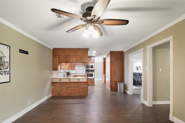 kitchen with brown cabinetry, dark wood-style floors, appliances with stainless steel finishes, a peninsula, and a sink