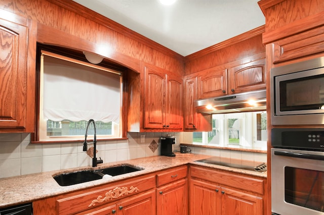 kitchen with under cabinet range hood, a sink, brown cabinets, decorative backsplash, and black appliances