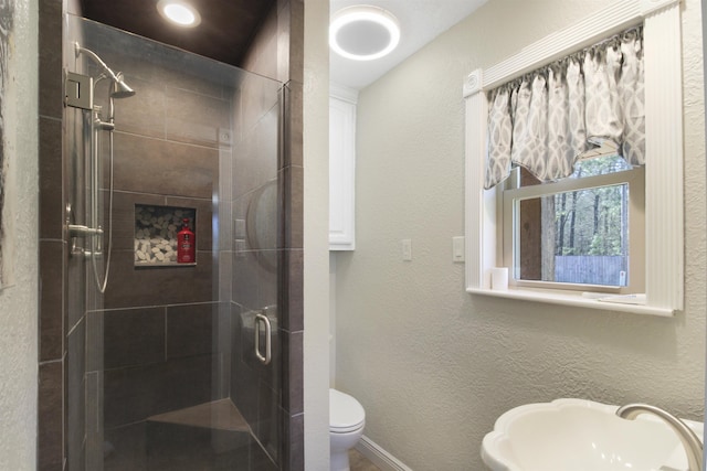 bathroom featuring baseboards, a textured wall, toilet, a shower stall, and a sink