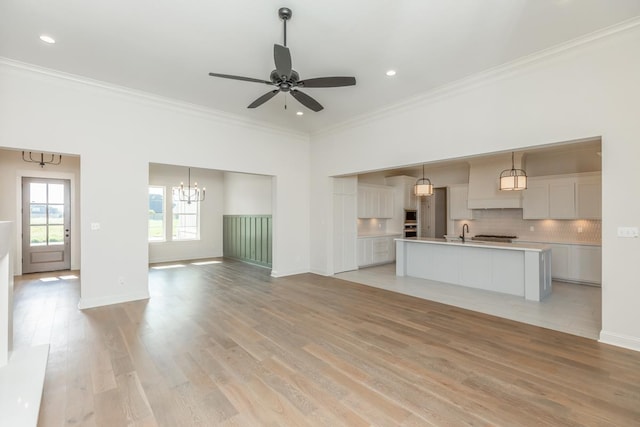 unfurnished living room with ornamental molding, sink, ceiling fan with notable chandelier, and light wood-type flooring