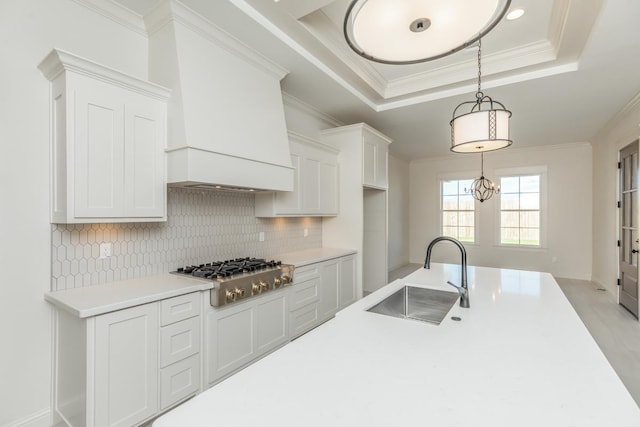 kitchen with stainless steel gas stovetop, sink, white cabinets, a tray ceiling, and crown molding