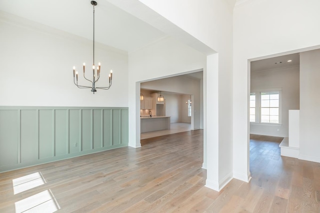 unfurnished dining area featuring ornamental molding, a notable chandelier, and light wood-type flooring