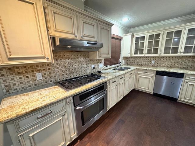 6845 Hialeah Dr, Beaumont, TX 77706 - kitchen with stainless steel appliances, under cabinet range hood, a sink, dark wood-style flooring, and glass insert cabinets