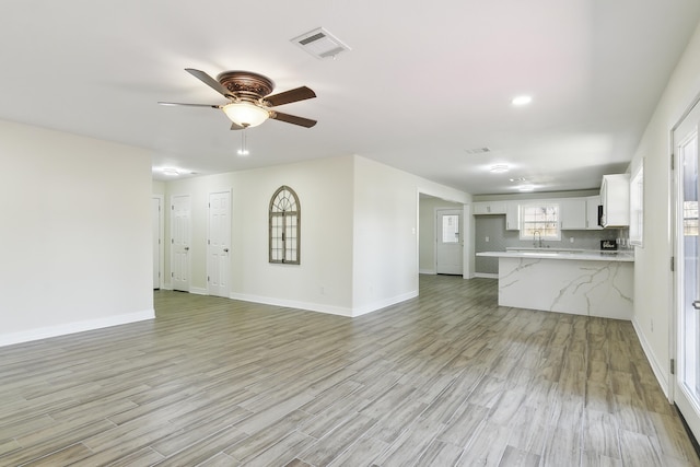 unfurnished living room with sink, ceiling fan, and light hardwood / wood-style flooring