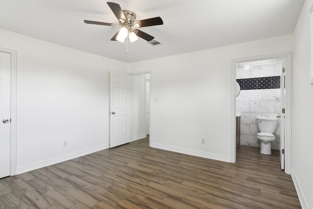 unfurnished bedroom with dark hardwood / wood-style flooring, tile walls, ceiling fan, and ensuite bath