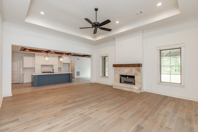 unfurnished living room featuring a stone fireplace, ornamental molding, light hardwood / wood-style floors, and a raised ceiling