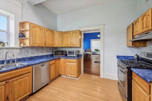 kitchen with appliances with stainless steel finishes, dark countertops, a sink, under cabinet range hood, and light wood-style flooring
