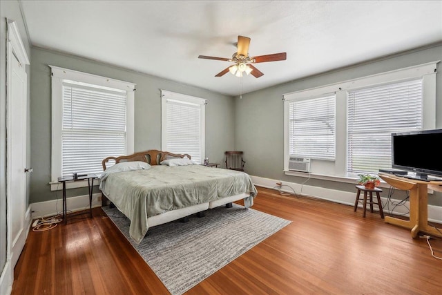 bedroom featuring a ceiling fan, baseboards, wood finished floors, and cooling unit