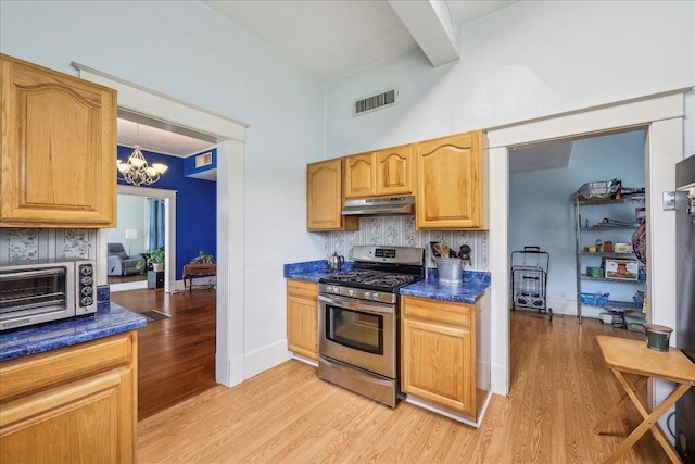 kitchen with visible vents, dark countertops, under cabinet range hood, light wood-style flooring, and gas stove