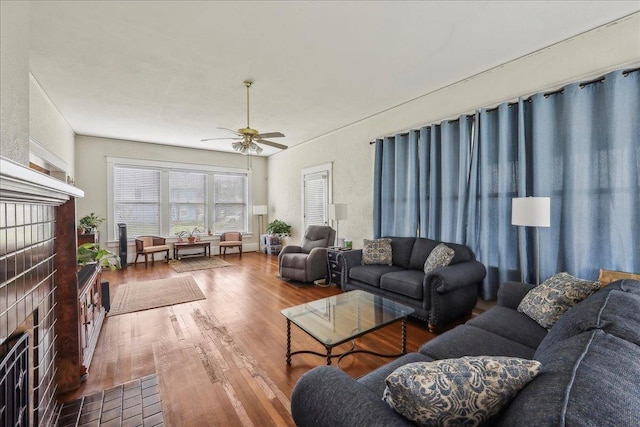 living area featuring a ceiling fan, a brick fireplace, and wood finished floors