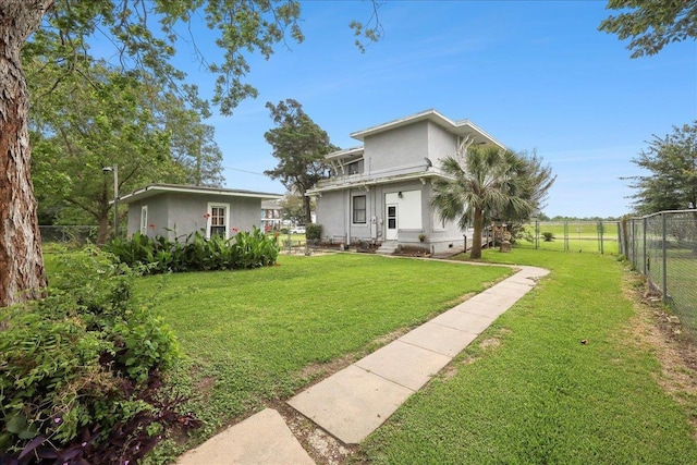 rear view of house with a yard, fence, and stucco siding