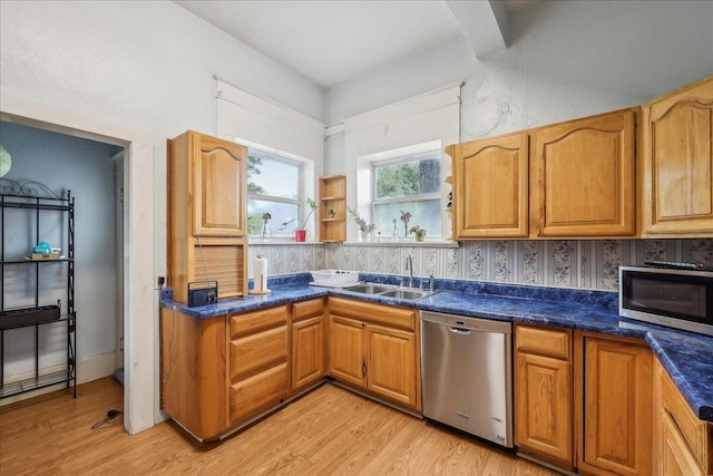 kitchen with brown cabinetry, dark countertops, a sink, light wood-style flooring, and stainless steel appliances