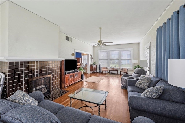 living area featuring ceiling fan, a tile fireplace, wood finished floors, and visible vents