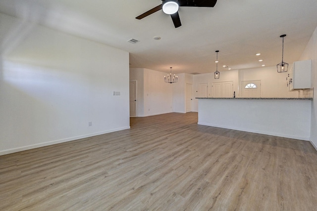 unfurnished living room featuring ceiling fan with notable chandelier and light hardwood / wood-style floors