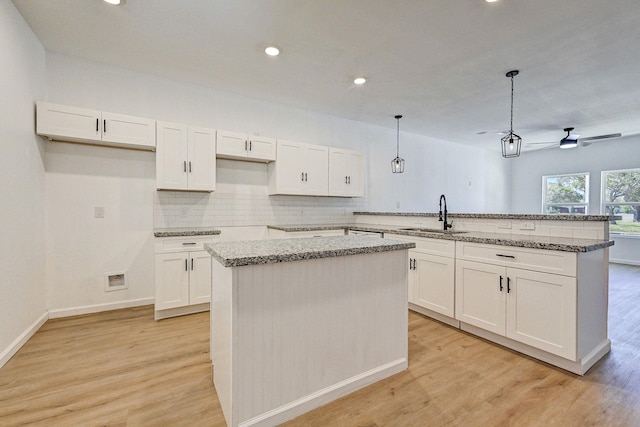 kitchen with pendant lighting, sink, ceiling fan, a kitchen island, and white cabinetry