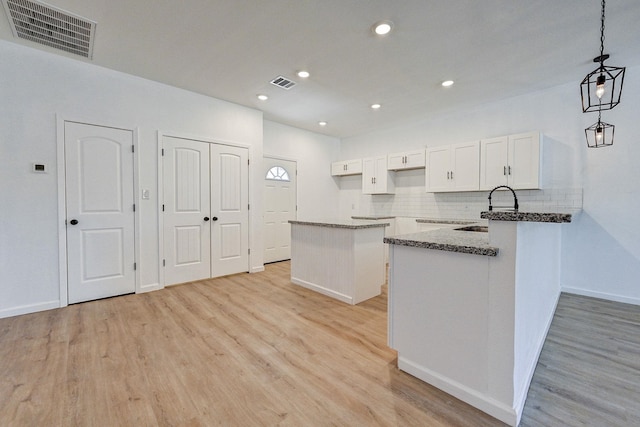 kitchen featuring sink, decorative light fixtures, light hardwood / wood-style flooring, a center island, and white cabinetry