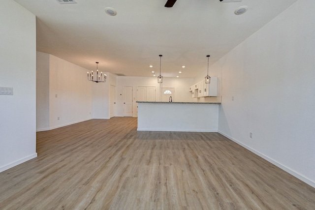 unfurnished living room with ceiling fan with notable chandelier and light hardwood / wood-style flooring