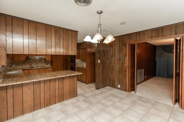 190 Magnolia Trl, Lumberton, TX 77657 - kitchen featuring under cabinet range hood, black electric cooktop, decorative backsplash, brown cabinetry, and wooden walls