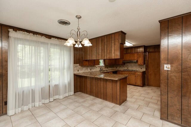 190 Magnolia Trl, Lumberton, TX 77657 - kitchen with a peninsula, brown cabinets, under cabinet range hood, decorative backsplash, and a chandelier