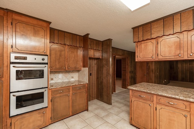 190 Magnolia Trl, Lumberton, TX 77657 - kitchen featuring white double oven, wooden walls, a textured ceiling, brown cabinetry, and light countertops