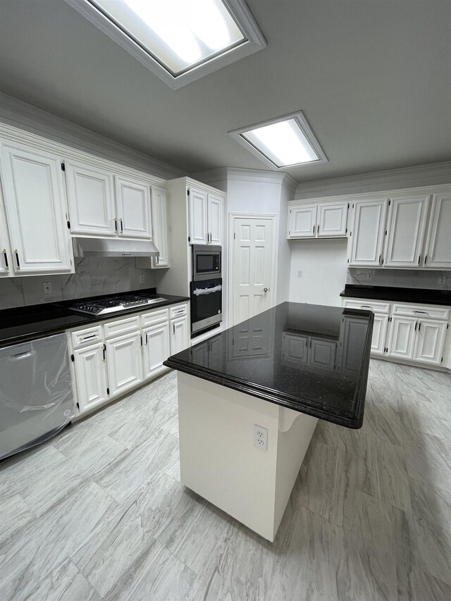 kitchen featuring appliances with stainless steel finishes, a kitchen island, white cabinetry, dark stone counters, and decorative backsplash