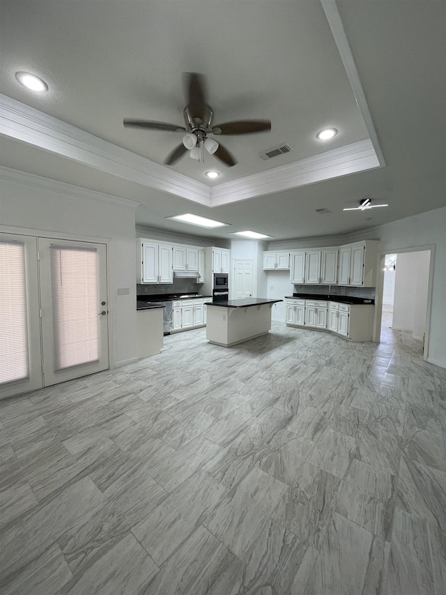 kitchen with ceiling fan, stainless steel microwave, a raised ceiling, crown molding, and white cabinetry