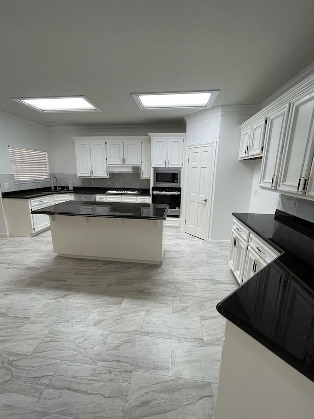 kitchen with stainless steel microwave, wall oven, white cabinetry, and a center island