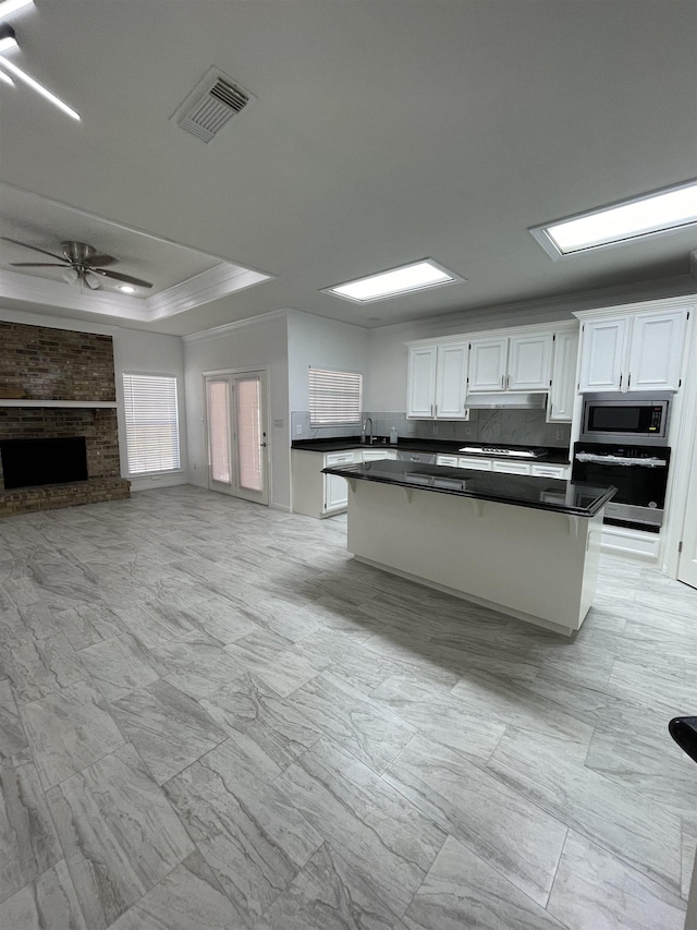 kitchen with ceiling fan, a fireplace, a raised ceiling, white cabinetry, and appliances with stainless steel finishes