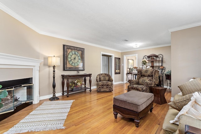 living room with ornamental molding, a glass covered fireplace, baseboards, and light wood finished floors