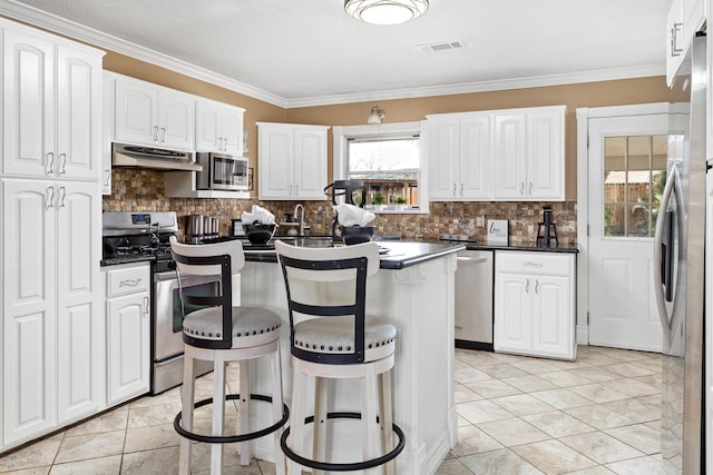 kitchen featuring stainless steel appliances, dark countertops, visible vents, under cabinet range hood, and a kitchen breakfast bar