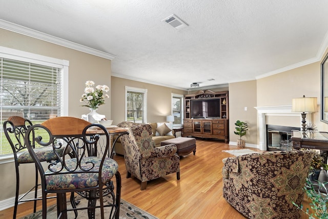 living room featuring a textured ceiling, a fireplace, visible vents, light wood-type flooring, and crown molding