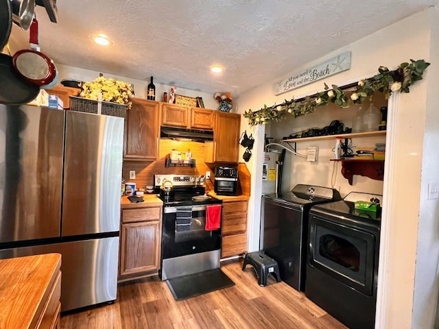 kitchen featuring tasteful backsplash, a textured ceiling, stainless steel appliances, washing machine and clothes dryer, and hardwood / wood-style floors