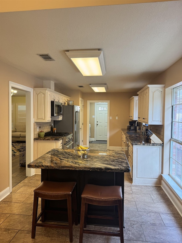 205 N Mayhaw Dr, Vidor, TX 77662 - kitchen with stainless steel appliances, tasteful backsplash, a kitchen island, dark stone countertops, and a kitchen bar